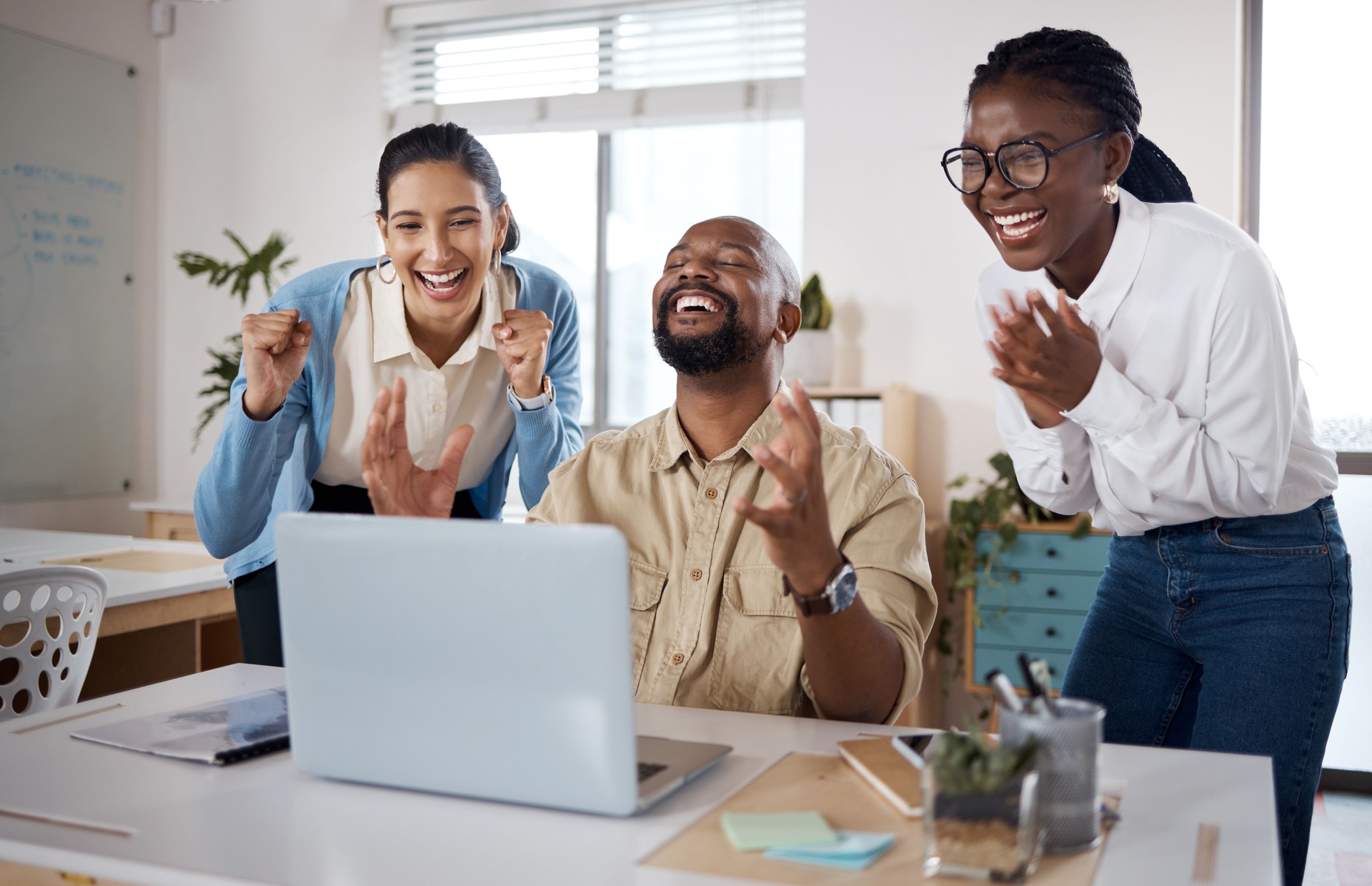 Shot of a group of businesspeople using a laptop and cheering in a modern office